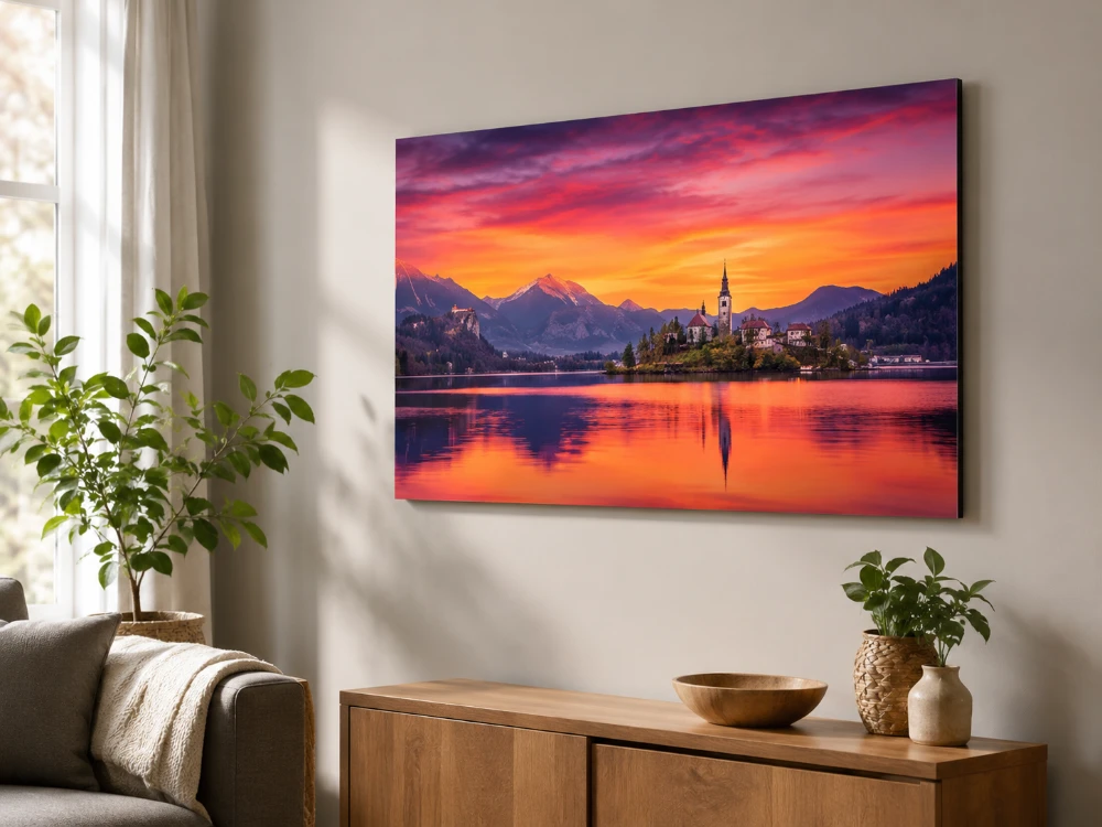 A vivid acrylic print of a fiery orange lake sunset with a church on an island, mounted above a wooden sideboard and glowing in soft daylight