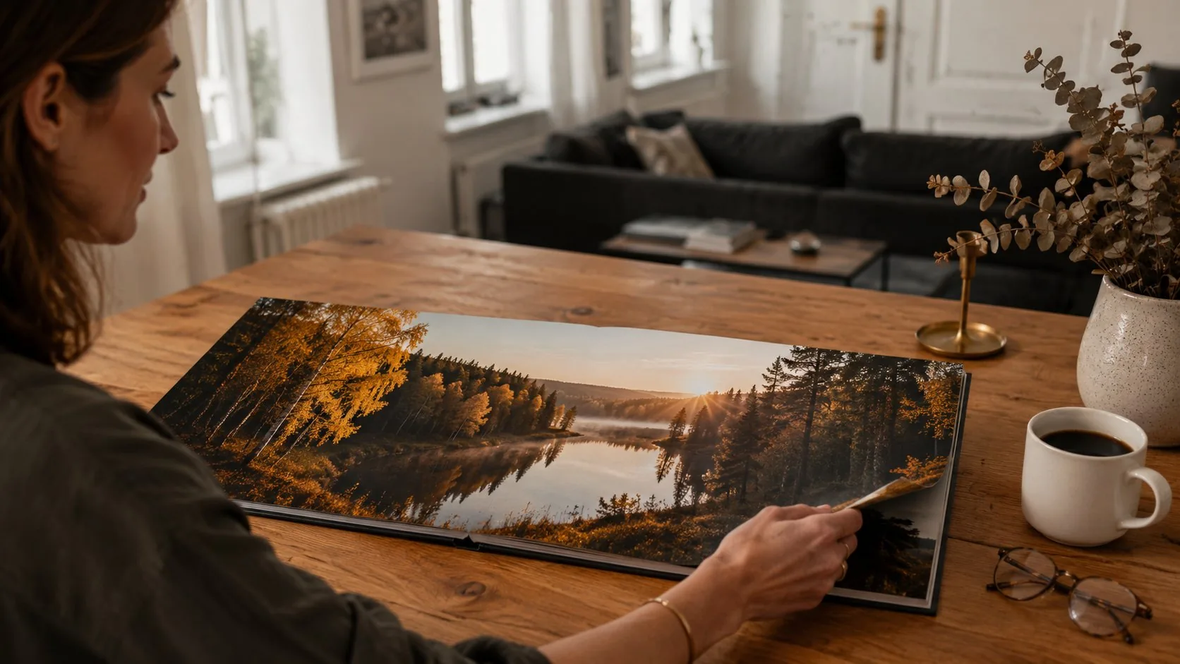 Woman browsing an open layflat photo book showing a panoramic autumn landscape across a seamless double-page spread