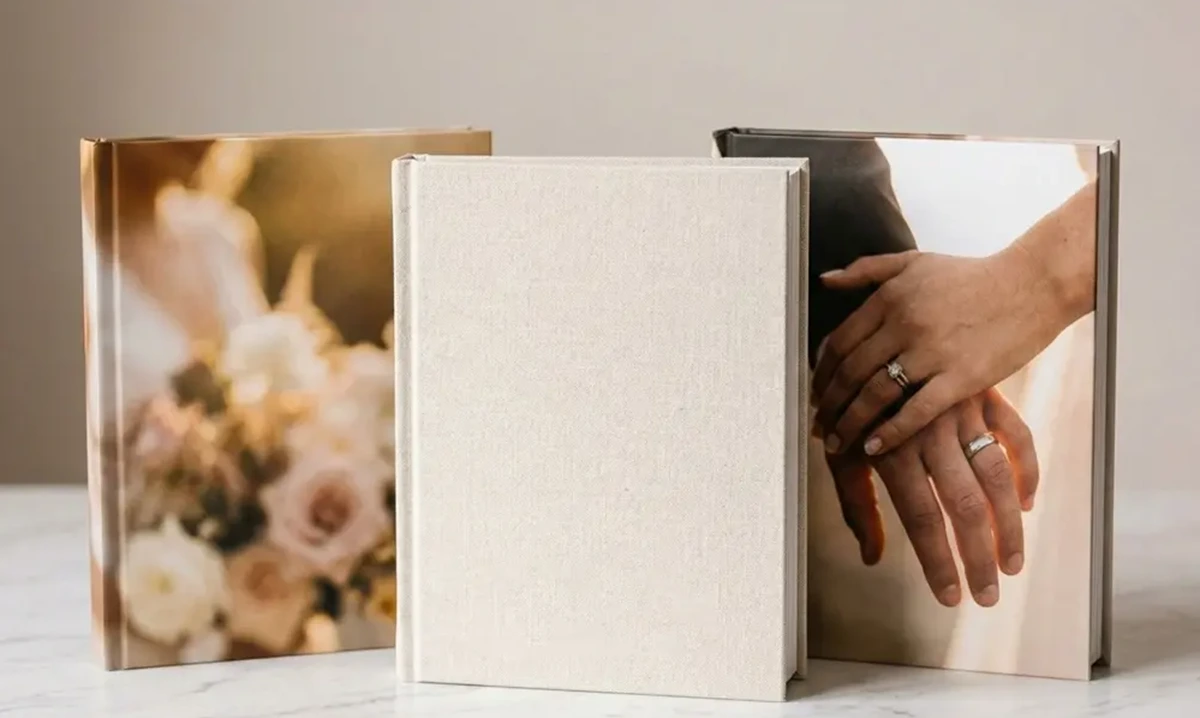 Open wedding scrapbook-style photo book showing photographs alongside a pressed flower, handwritten note and printed menu card on cream pages