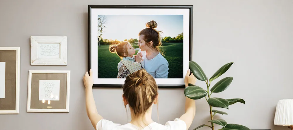 How to arrange photos on a wall: a woman hanging a large canvas print on the wall