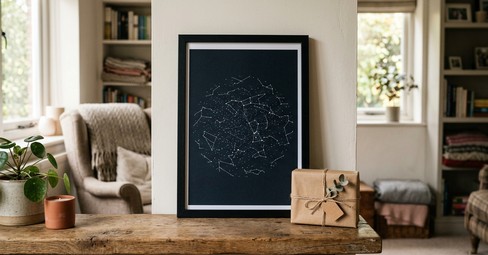 A framed black star map print hanging on a green living-room wall beside a floor lamp in the evening