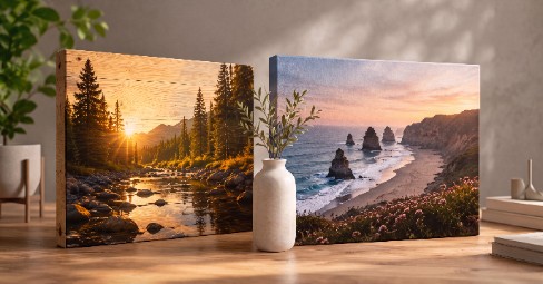 A wood print of a mountain-and-lake sunset with visible timber grain beside a gallery-wrapped canvas print of a lakeside jetty at sunset, displayed on a living-room wall